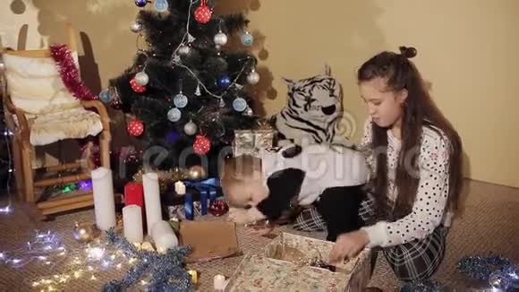 那个小男孩和他妹妹在装饰精美的圣诞树旁打开新年礼物盒孩子是视频的预览图