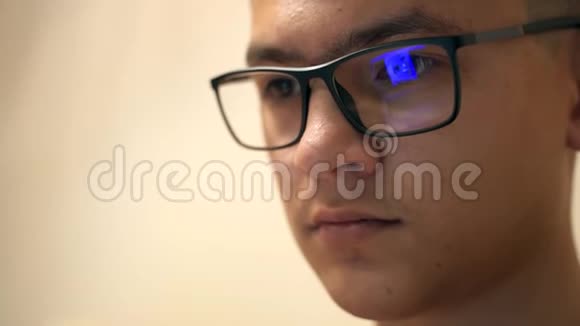 在现代办公室里戴眼镜晚上通过笔记本电脑工作的年轻时髦男人的特写镜头男性的特写镜头视频的预览图