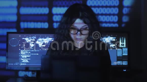 戴眼镜的女黑客程序员正在计算机安全中心工作里面装满了显示屏二元视频的预览图