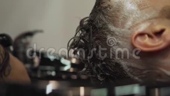 理发店一个年轻人从一个留胡子的男人那里得到理发和护发服务他的头上绑着头发视频的预览图