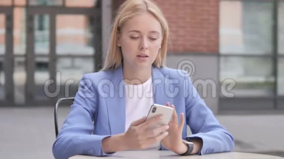 年轻的女商人使用智能手机户外坐着视频的预览图