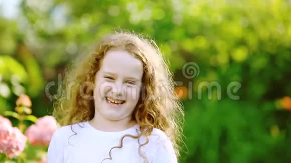 一个穿着白色T恤的小卷曲女孩微笑着愤怒着任性着夏天在公园里挥舞着拳头视频的预览图