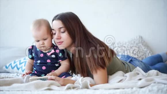 漂亮的女人和她可爱的宝宝躺在床上用手机看动画片视频的预览图