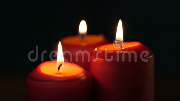 三支厚厚的红色圣诞蜡烛在黑色背景上燃烧视频的预览图