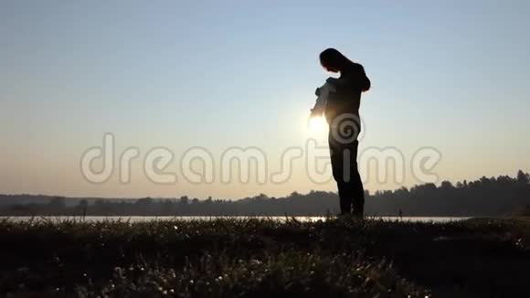 一个虔诚的孕妇在秋天的日落时与婴儿一起身体服视频的预览图