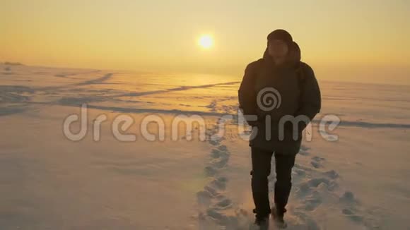傍晚一个人穿过白雪覆盖的沙漠夕阳照在雪上视频的预览图