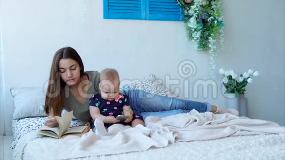 一位年轻的母亲和她的小女儿躺在床上看书视频的预览图
