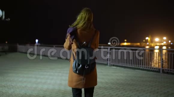 迷人的年轻女性在夜间在街上散步时使用智能手机慢动作视频的预览图