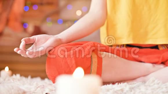 特写一个女孩被家里的蜡烛包围在窗前在莲花的位置冥想手指在旁边的泥地上视频的预览图