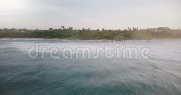 无人机锁定拍摄美丽平静的海浪与泡沫到达风景如画的海岸与热带树木和房子视频的预览图