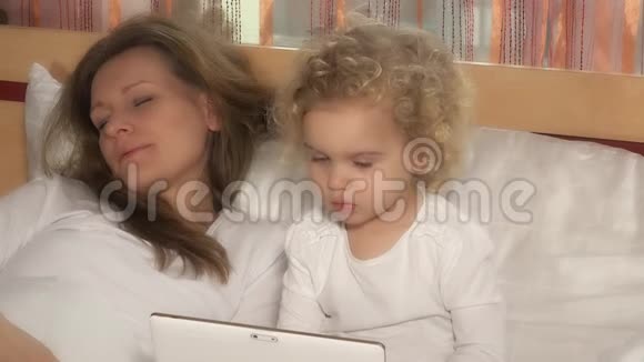 漂亮的女孩子在妈妈睡觉的时候看着平板电脑视频的预览图