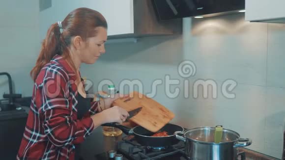 女孩在锅里炒胡萝卜女人在家里的厨房做饭做烤年轻女子加胡萝卜的肖像视频的预览图