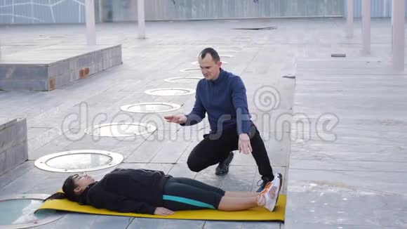 与户外私人教练一起健身女人躺在黄色的垫子上骑自行车教练纠正正确视频的预览图