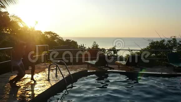 年轻的幸福夫妇在日落时分在度假胜地的游泳池里跳跃慢慢地在水下溅起水滴视频的预览图