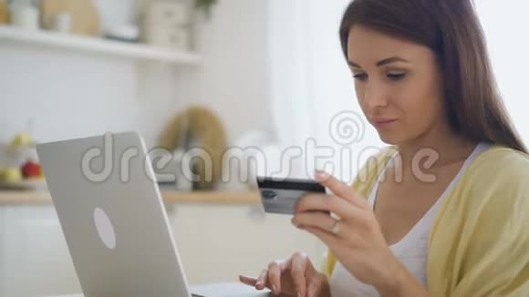 年轻女子坐在家里拿着笔记本电脑用信用卡支付购买费用视频的预览图
