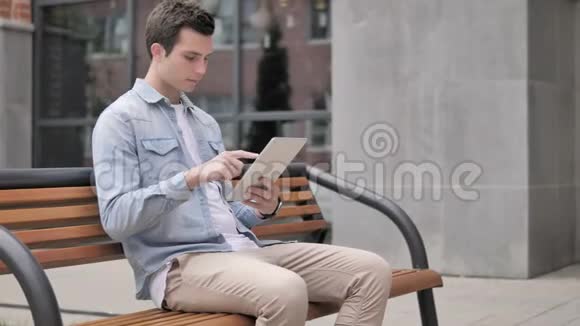 休闲青年坐在户外使用平板电脑视频的预览图