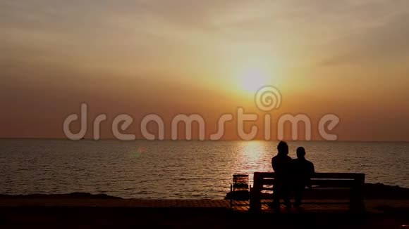 坐在长凳上的男人和女人看着大海上的日落视频的预览图