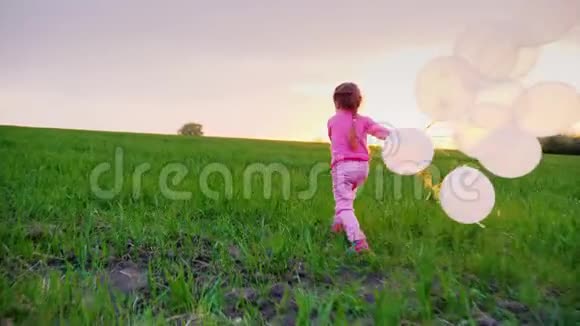 穿着带气球的粉红色衣服的小女孩我沿着绿色的草地玩耍走向日落孩子们梦想快乐视频的预览图