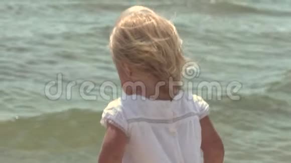 美丽的小女孩沿着海滨散步在海岸穿白色裙子的小女孩慢动作视频的预览图