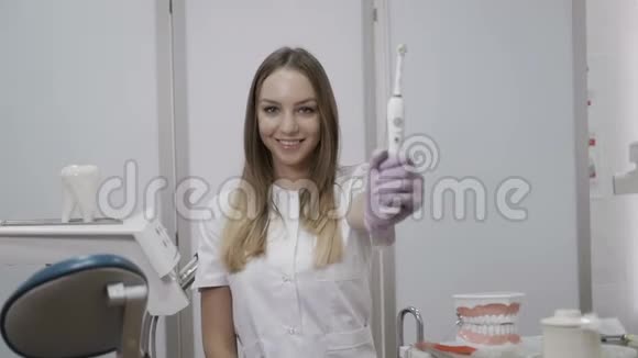 美丽的牙医在相机上展示了钻床和电动牙刷视频的预览图