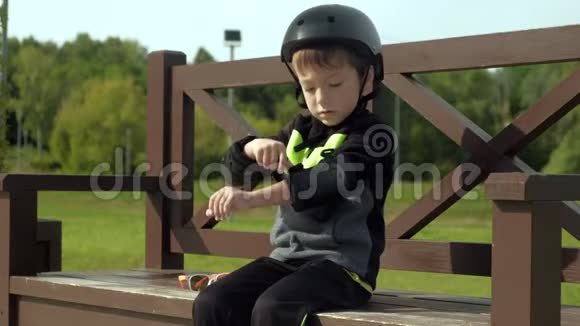 一个学龄前男孩坐在公园的长凳上把保护放在他的头膝盖和手臂上夏季视频的预览图