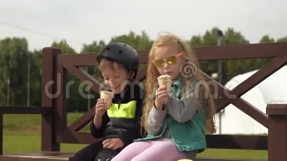 一个男孩和一个女孩坐在公园的长凳上吃冰淇淋夏季视频的预览图