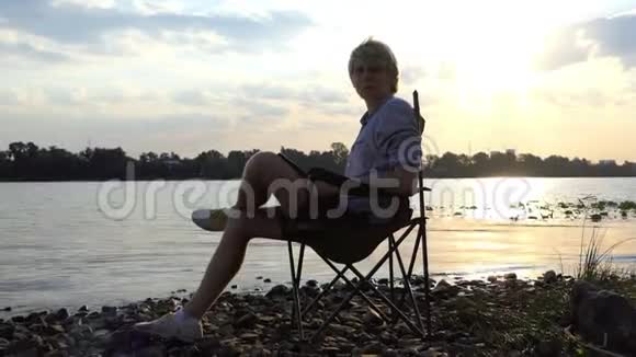 年轻人坐在椅子上把他的杰作写在河岸上视频的预览图