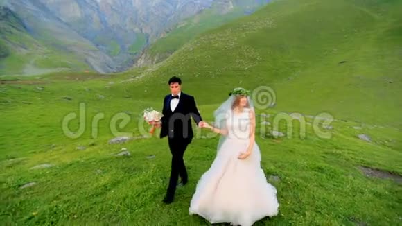在美丽的山峦背景下新婚夫妇晚上在草地上散步视频的预览图