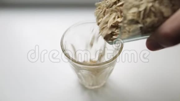 健康素食早餐燕麦粥一个白人的手把一个杯子里的大燕麦片倒进另一个杯子里视频的预览图