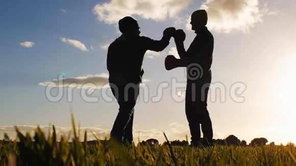 户外拳击训练教练低角度拍摄的对手剪影拳击手套在夕阳的天空视频的预览图