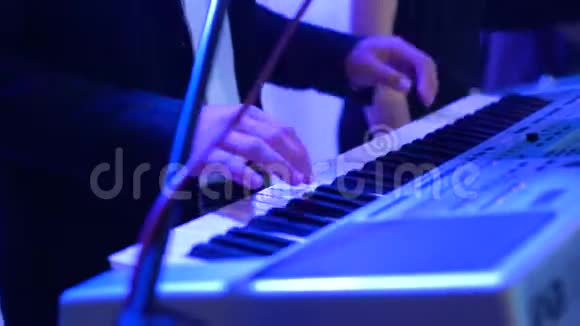 男子双手在彩色舞台灯光下弹电钢琴特写镜头视频的预览图