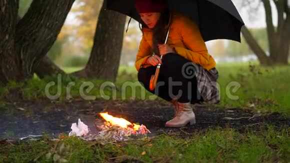 凄冷的女人在雨中坐在森林里的炉火旁视频的预览图
