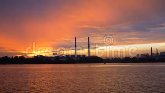日落背景下从河上的船上俯瞰傍晚的城市大型管道的剪影视频的预览图