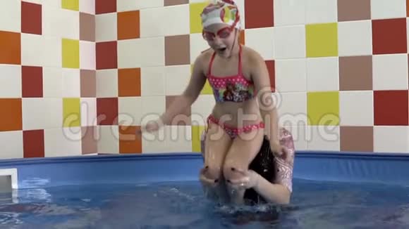 小女孩从教练的肩膀上潜入游泳池视频的预览图