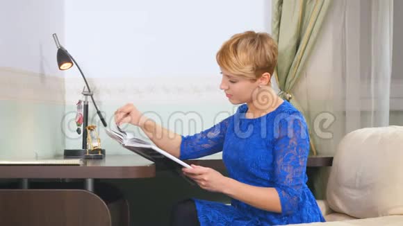 穿蓝色衣服的年轻女子在家看杂志视频的预览图
