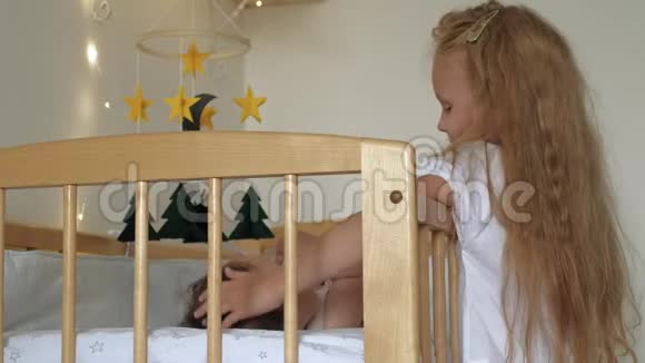 女孩学龄前女孩和一个孩子站在婴儿床旁给她舒缓照顾小妹妹视频的预览图