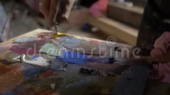 艺术家调色板刀混彩油画在调色板上握着他的手特写在车间里4K视频的预览图