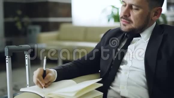 在酒店坐在扶手椅上时一位自信的商人在笔记本电脑上聊天写笔记视频的预览图