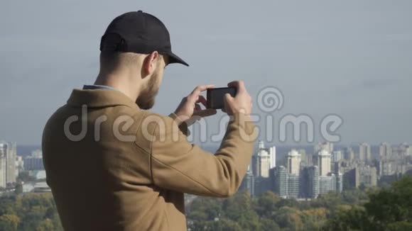 戴帽子的年轻人在智能手机上拍摄城市全景照片视频的预览图