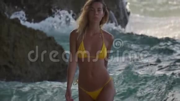 穿着黄色比基尼的漂亮女人在海滩上迎着大海的波涛散步视频的预览图