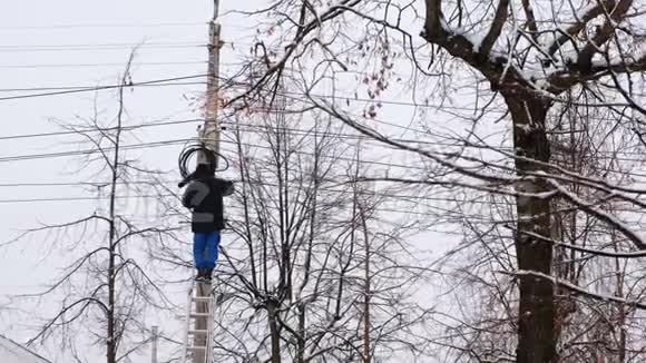 冬季城市电力线路的人修站在梯子上手里拿着电线后视图视频的预览图