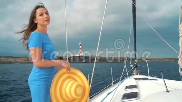 穿着黄色帽子和蓝色裙子的女人站在游艇上与某人交谈并指向岸上的灯塔视频的预览图