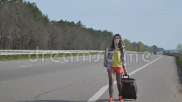 带着手提箱和背包的年轻女孩走在路边视频的预览图