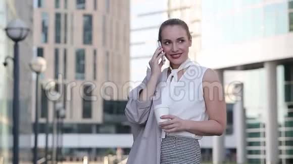 年轻的商务女性拿着一杯咖啡在智能手机上交谈站在市中心视频的预览图