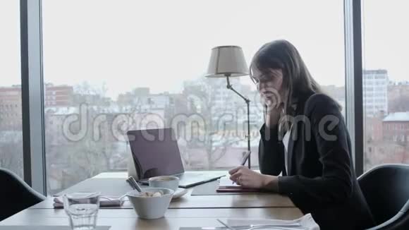 漂亮的女人在笔记本上做笔记年轻的女商人坐在木桌旁的咖啡店里桌子上是灰色的视频的预览图