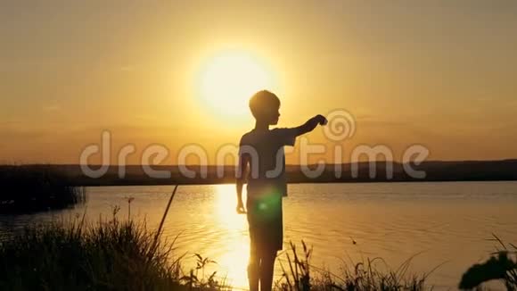 橙色夕阳背景下一个男孩在水里扔石头的剪影视频的预览图