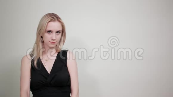一个穿着黑色裙子的金发女孩在一个与世隔绝的白色背景下表现出情感视频的预览图