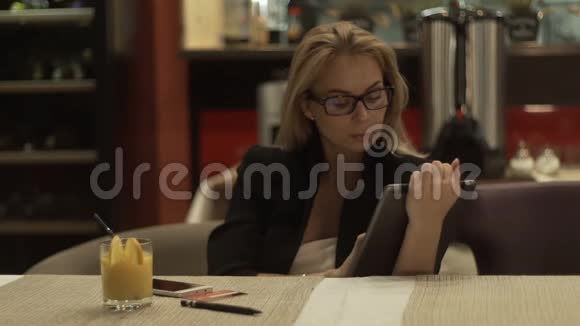 一位戴眼镜的年轻女士坐在咖啡馆里在平板电脑上打字视频的预览图