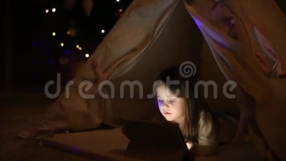 一个躺在地板上的小女孩抱着她坐在圣诞树背景下的帐篷里视频的预览图