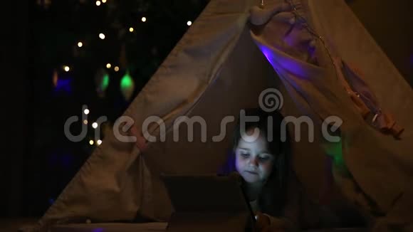 一个躺在地上的小女孩坐在一个圣诞树背景下的帐篷里进入了一个搜索视频的预览图